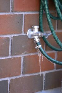 An exterior leaking water tap connected to a hose on bricks