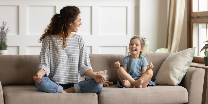 Young mom and child playing on couch yoga position