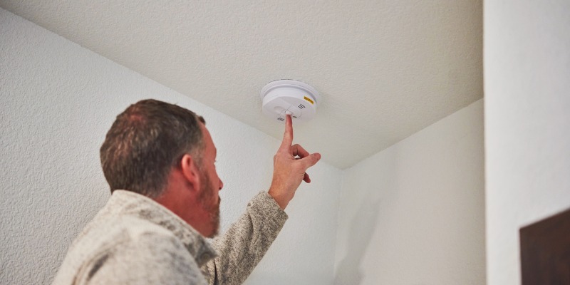 Man holding button on carbon monoxide detector - How do carbon monoxide alarms work?   